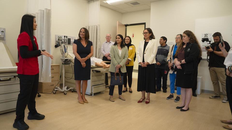 People stand in a clinical room with a person in a red uniform speaking to them.