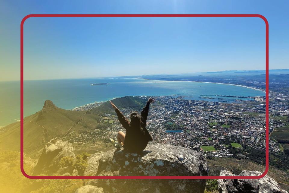 Student sitting on a cliff with her hands in the air in a foreign country.