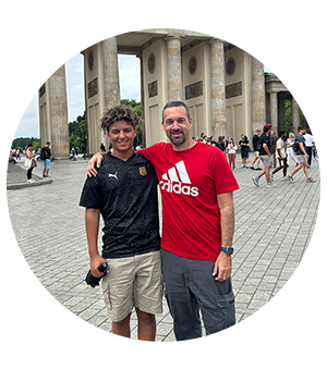 Two people stand smiling in front of the Brandenburg Gate in Berlin.